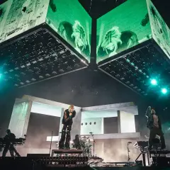 Energetyczny linkin park opener na scenie. Wokalista śpiewa, zespół gra, a nad nimi ogromne ekrany z zielonymi wizualizacjami.