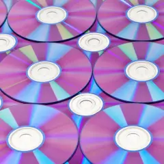 Stos płyt CD/DVD z fioletowo-niebieskimi refleksami, widoczne środkowe otwory.