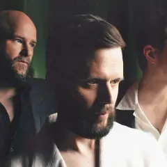 Trzech mężczyzn w garniturach, przygotowujących się do koncertu White Lies.