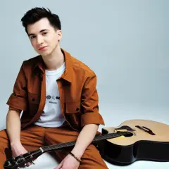 Marcin Patrzałek, młody muzyk, siedzi z gitarą, gotowy na koncert.