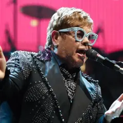 Elton John w błyszczącej marynarce śpiewa na jednym ze swoich niezapomnianych koncertów.