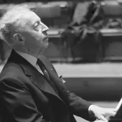 Artysta w garniturze, polski pianista jazzowy, pochyla się nad fortepianem, skupiony na grze.