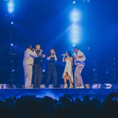 Zespół Pentatonix występuje na scenie w blasku niebieskich świateł, śpiewając do mikrofonów.