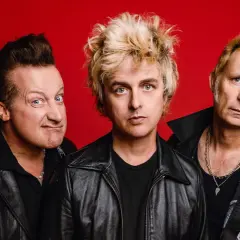 Trzech członków zespołu Green Day na czerwonym tle, w skórzanych kurtkach.