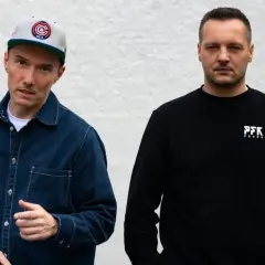 Dwóch członków Paktofoniki, jeden w czapce z daszkiem i granatowej kurtce, drugi w czarnej bluzie z logo PFK.