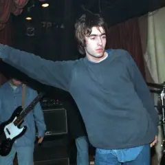 Liam Gallagher z Oasis śpiewa na scenie, w tle basista i perkusja. To klasyczne oasis utwory.