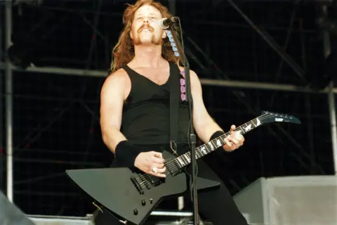 James Hetfield z Metalliki gra na czarnej gitarze na scenie.