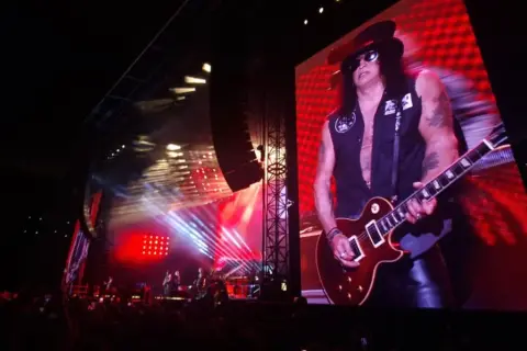 Slash z Guns N' Roses gra na gitarze na wielkim ekranie podczas koncertu w Warszawie.