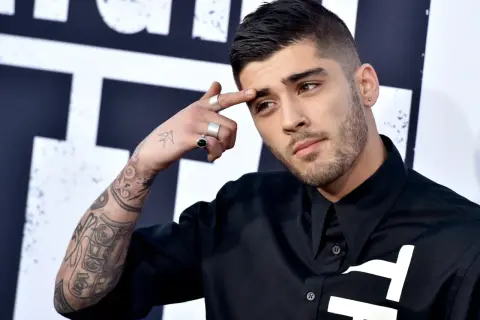 Zayn Malik, były członek One Direction, z tatuażami na ramieniu i palcami ozdobionymi pierścionkami, dotyka czoła.