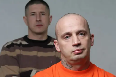 Dwóch mężczyzn, jeden z przodu w pomarańczowej koszulce i tatuażem na szyi, drugi z tyłu w bluzie w paski.