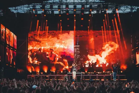 Koncert na festiwalu z ognistą scenografią i tłumem widzów.