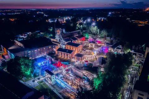 Nocny festiwal z kolorowymi światłami na terenie postindustrialnym. Ludzie bawią się na koncertach i stoiskach. To świetne miejsce na **carbon festival**!