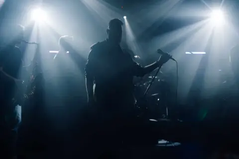 Zespół muzyczny na scenie, wokalista z mikrofonem, saksofonista, światła sceniczne.