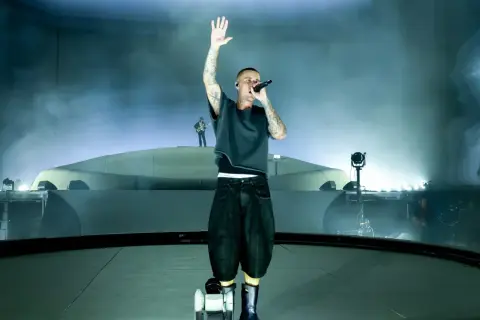 Justin Bieber śpiewa na scenie z podniesioną ręką, otoczony mgłą i światłami.