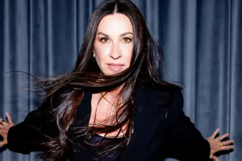 Alanis Morissette z rozwianymi włosami, w czarnej marynarce, gotowa na koncert.