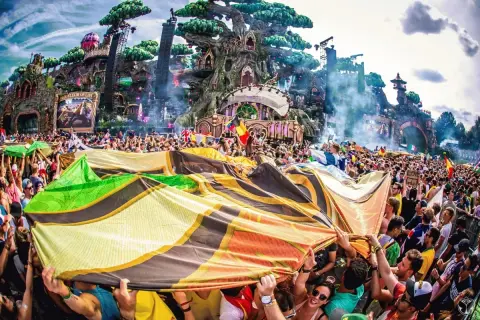 Tłum ludzi na festiwalu Tomorrowland, trzymający kolorową flagę, z imponującą sceną w tle.