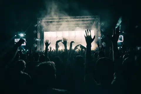 Tłum ludzi z podniesionymi rękami na koncercie przed sceną oświetloną światłami i dymem.