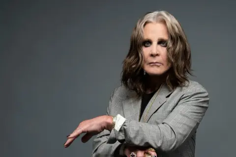 Ozzy Osbourne w szarej marynarce, z charakterystycznym makijażem oczu. Ikona rocka, której ozzy osbourne utwory wciąż inspirują.
