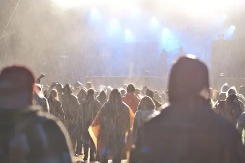 Tłum ludzi na festiwalu w deszczu, widok na scenę z oświetleniem.