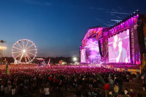 Koncert na Pol'and'Rock Festival z wielkim tłumem, sceną i diabelskim młynem w tle.