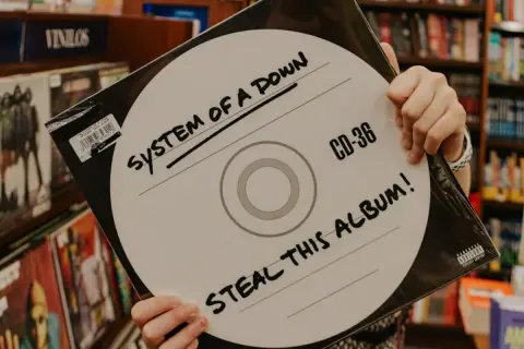 Ręce trzymają okładkę płyty System of a Down "Steal This Album!". Wybór między winylami a CD.