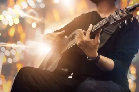 Mężczyzna grający na gitarze akustycznej na tle rozmytych świateł.