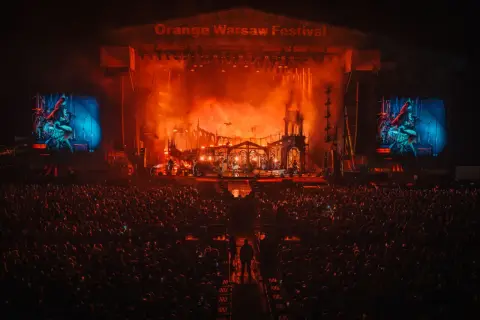 Koncert na Orange Warsaw Festival. Tłum ludzi pod sceną, na której trwa widowiskowe show z efektami pirotechnicznymi.