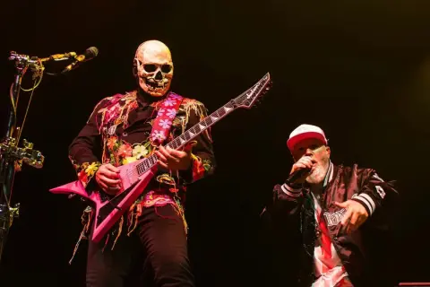 Muzyk w masce czaszki gra na różowej gitarze, wokalista w czapce śpiewa na scenie podczas impact festival.