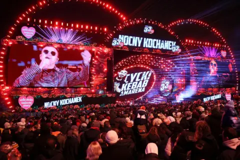 Koncert WOŚP 2026: tłumy ludzi pod sceną, na ekranach artyści, czerwone światła i serca WOŚP.