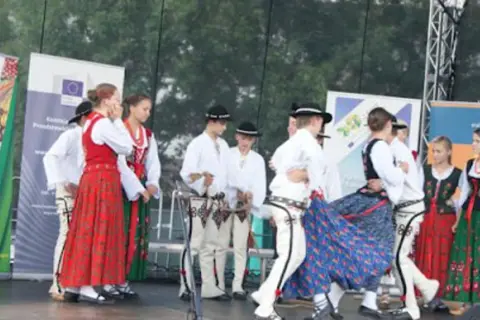 Grupa ludzi w tradycyjnych strojach ludowych tańczy na scenie.