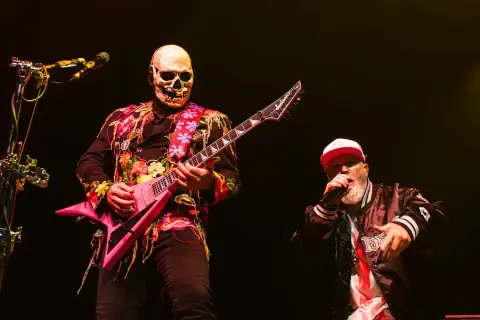 Muzyk w masce czaszki gra na różowej gitarze, a wokalista w czapce śpiewa na koncercie Limp Bizkit.