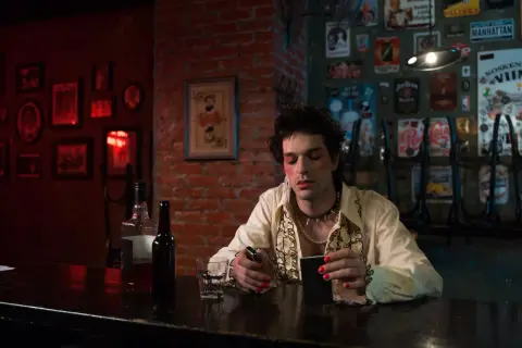 Młoda osoba z makijażem i biżuterią, siedząca przy barze, odzwierciedla ducha punk subkultury.