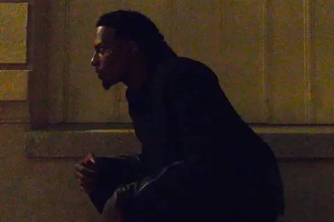 Playboi Carti w Polsce, siedzi w mroku, czekając na coś.
