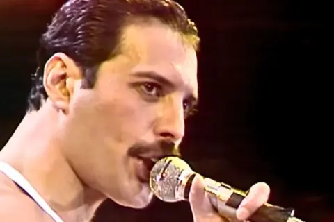 Freddie Mercury śpiewający do mikrofonu na scenie.