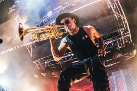 Timmy Trumpet gra na trąbce na scenie podczas koncertu.