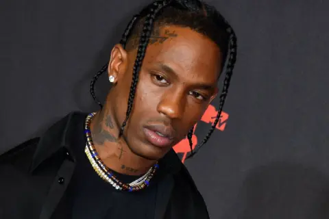 Travis Scott w czarnej koszuli i z warkoczami, z naszyjnikami i tatuażami na szyi.