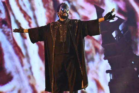 The Weeknd w czarnej, zdobionej masce i stroju, śpiewa na koncercie.