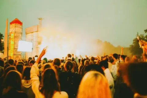 Tłum ludzi na koncercie, uniesione ręce, scena z oświetleniem. Tak wyglądają juwenalia, czyli święto studentów.