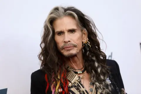 Steven Tyler z kolorowymi pasemkami we włosach, w czarnej marynarce i z biżuterią.