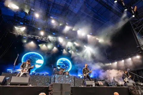 Zespół Bullet For My Valentine gra na scenie podczas koncertu, w tle niebieskie ekrany i światła.