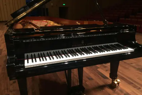 Czarny fortepian Steinway & Sons z otwartą klapą, na drewnianej scenie.