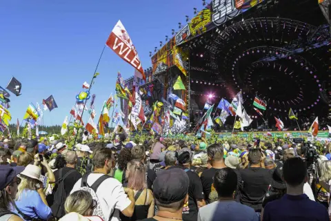 Tłum ludzi na festiwalu muzycznym z flagami i sceną w tle.