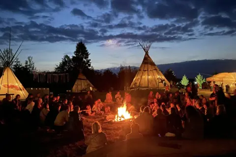 Ludzie siedzą przy ognisku pod namiotami tipi, tworząc atmosferę jednego z wielu festiwali na świecie.