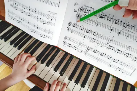 Dziecko uczy się gry na keyboardzie, ćwicząc nuty z podręcznika. Zielony ołówek zaznacza fragment do nauki.