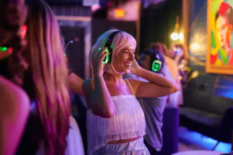 Kobieta w słuchawkach z podświetlanymi na zielono nausznikami tańczy na imprezie silent disco.