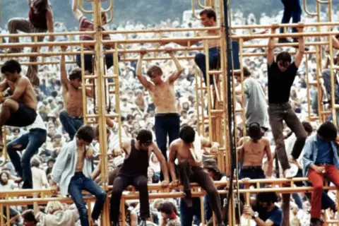 Ludzie wspinający się na żółtą konstrukcję podczas festiwalu Woodstock 1969.