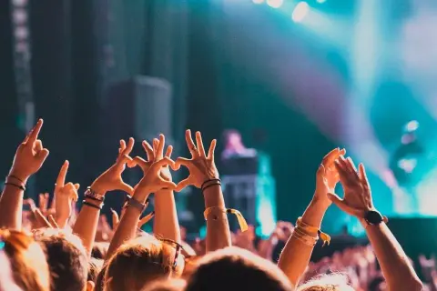 Tłum na letnim festiwalu, ręce w górze tworzą serca i gesty radości. Światła sceny tworzą magiczną atmosferę.