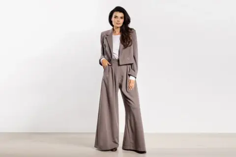 Kobieta w eleganckim, szarym garniturze z szerokimi spodniami i krótką marynarką.