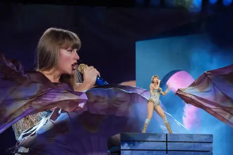 Taylor Swift na Taylor Swift The Eras Tour w błyszczącym stroju, z wielkim fioletowym materiałem unoszącym się wokół niej.