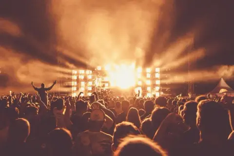 Tłum ludzi na festiwalu muzycznym, scena z jasnymi światłami i dymem.